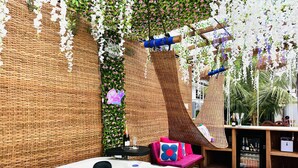 Un bain à remous agrémenté d’un fauteuil en osier et d’une table sur laquelle sont posées des bouteilles, le tout entouré d’un mur décoré de plantes suspendues et d’un néon.
