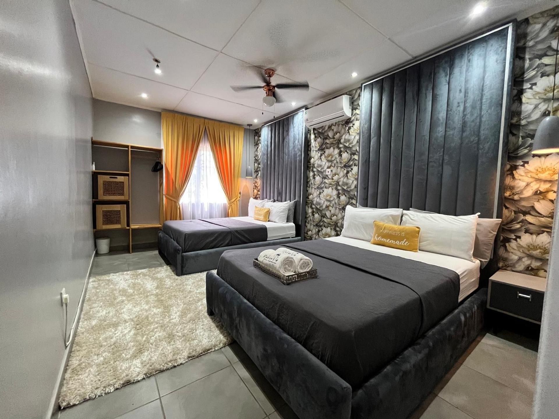 Un dormitorio moderno con dos camas, un ventilador de techo y un ventanal con cortinas.