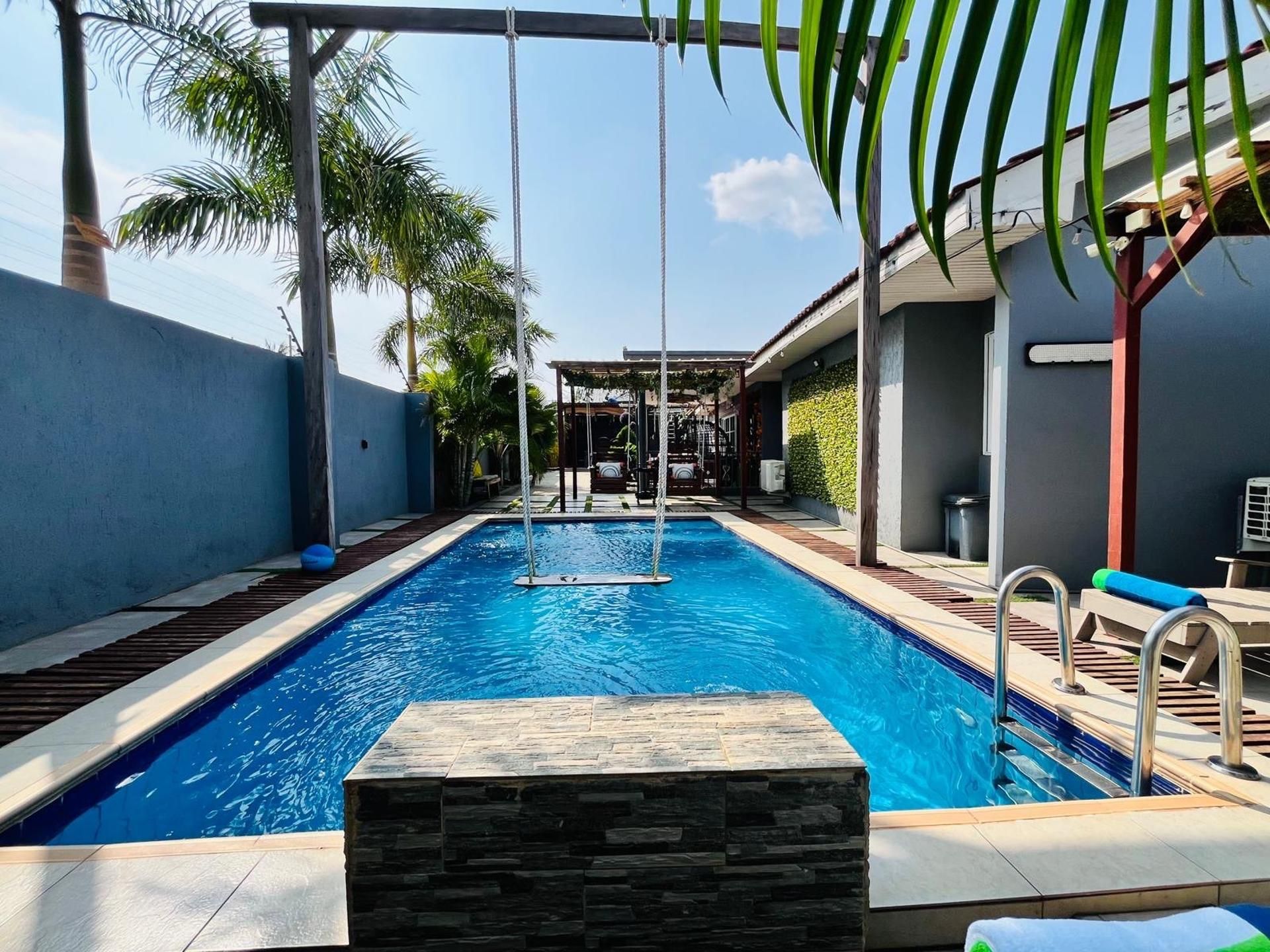 Una piscina con detalles en pared de piedra, una zona de columpios y palmeras.