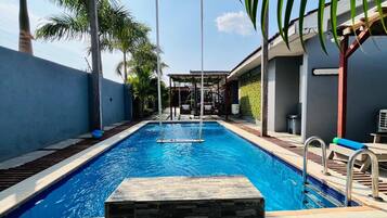 Una piscina con detalles en pared de piedra, una zona de columpios y palmeras.