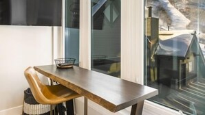Un interior moderno con una mesa de madera y una silla, un ventanal con vistas a un paisaje nevado, y un televisor de pantalla plana negro montado en la pared.