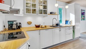 A modern kitchen with white cabinets, a wooden countertop, a built-in stove, a sink, and a window providing natural light. - 3 bedroom beautiful home in Vig (Vig)