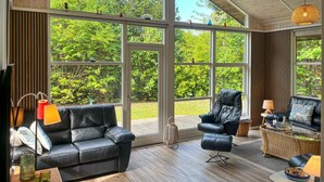 A spacious living room with large windows, a leather sofa, a black armchair, and a wicker side table. - 3 bedroom beautiful home in Vig (Vig)
