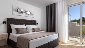 A modern bedroom with a large bed, a headboard with circular mirrors, a side table, and a view of a garden through a sliding glass door.
