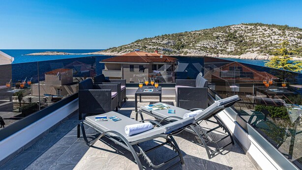 A rooftop terrace with lounge chairs, a table with drinks, and a view of the sea and hills.