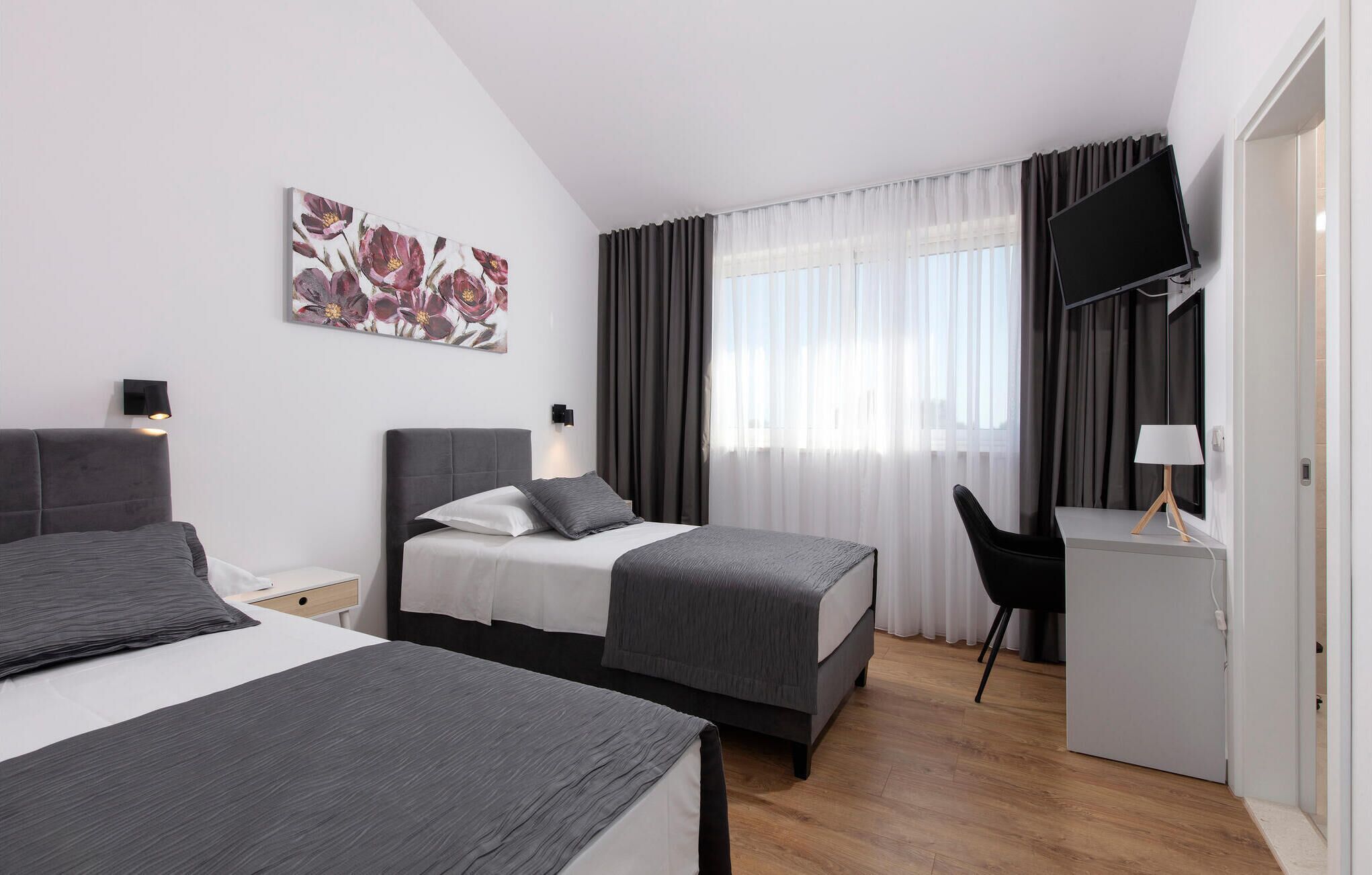 A modern hotel room with two beds, a desk with a chair, a TV, and a painting on the wall.
