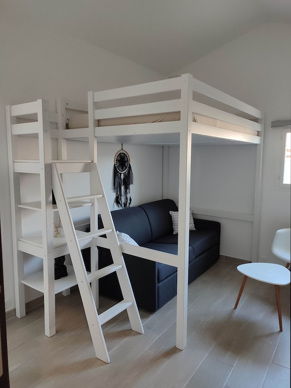 Et værelse med køjeseng, en stige, en mørk sofa, en drømmefanger og en hvid stol.