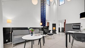 A modern living room with a grey sofa, a round white table, and a black armchair. There is a fireplace, a TV, and a kitchen area with an oven. - Gorgeous home in Grenaa with kitchen (Grenaa)