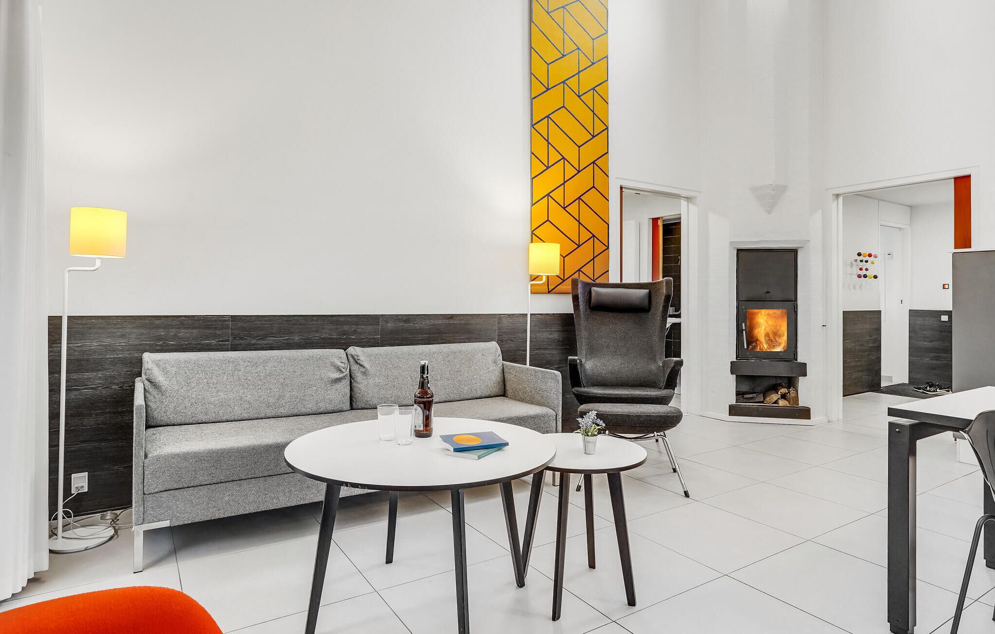 Een moderne woonkamer met een grijze bank, twee ronde tafels, een zwarte fauteuil en een open haard.