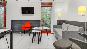 A modern living room with a sofa, a dining table, and a bright orange chair. A flat-screen TV is mounted on the wall, and there is a window with a view of trees. - Nice home in Grenaa with kitchen (Grenaa)