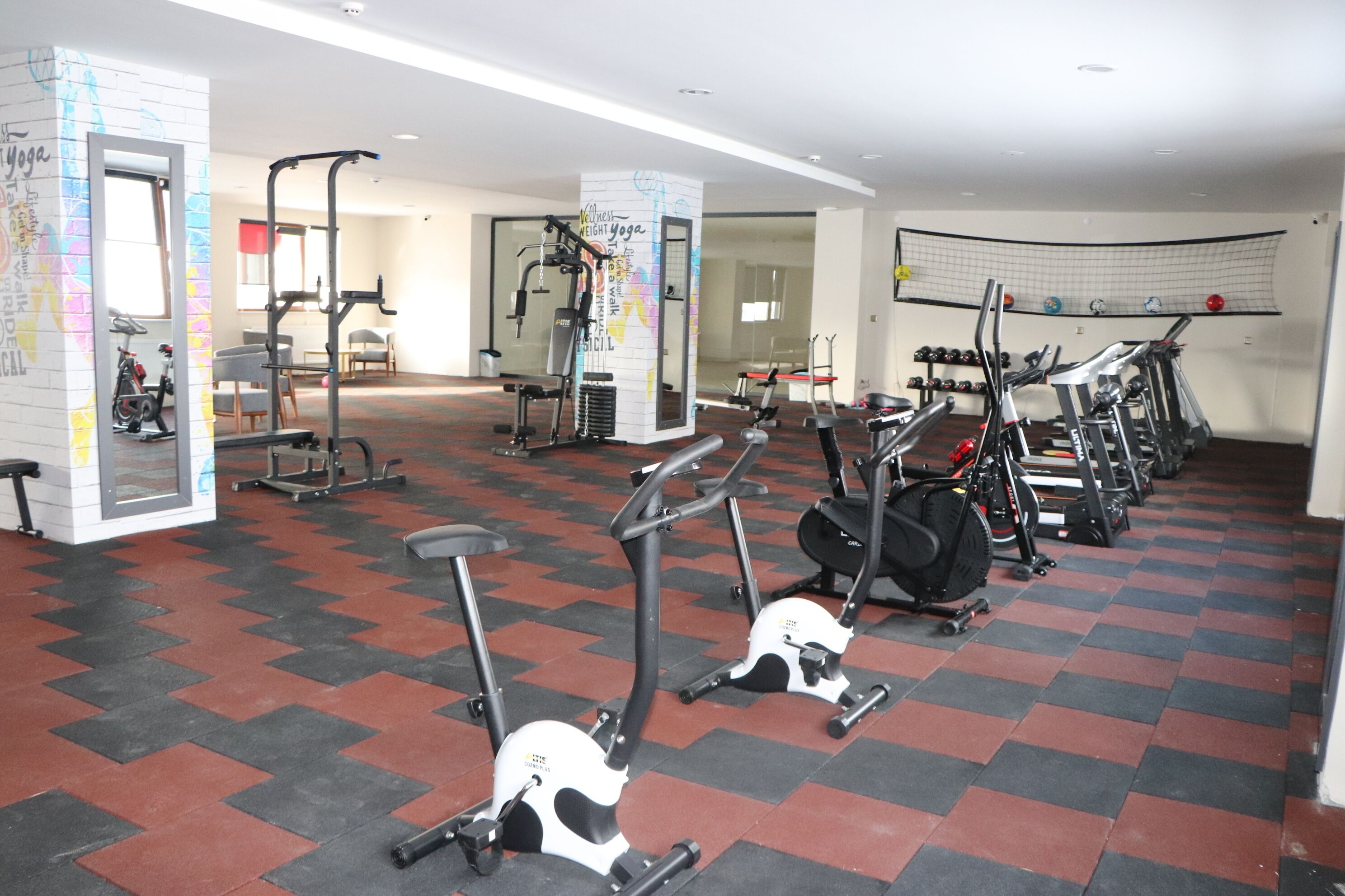 Ett gym med olika träningsmaskiner, en vägg täckt med speglar och ett mönstrat golv.