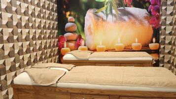 A spa room with a wooden bed, multiple candles, and a poster of a stone bath surrounded by flowers.
