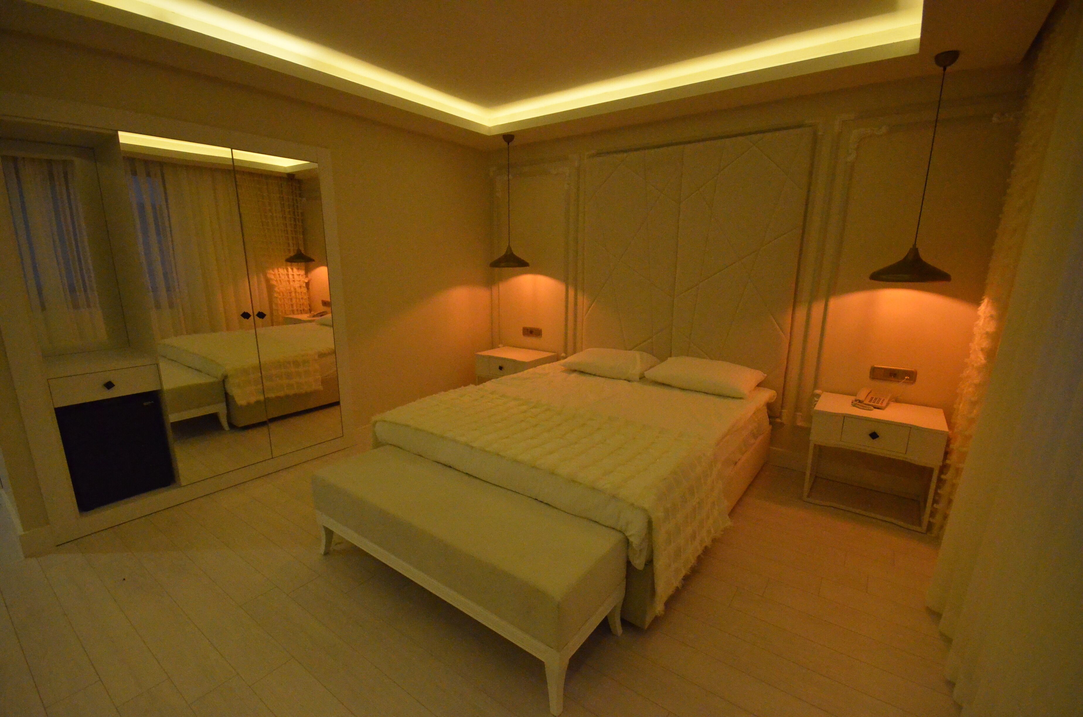 Une chambre à coucher comprenant un lit, des tables de chevet, un banc, un miroir et une armoire.