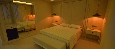 Une chambre à coucher comprenant un lit, des tables de chevet, un banc, un miroir et une armoire.