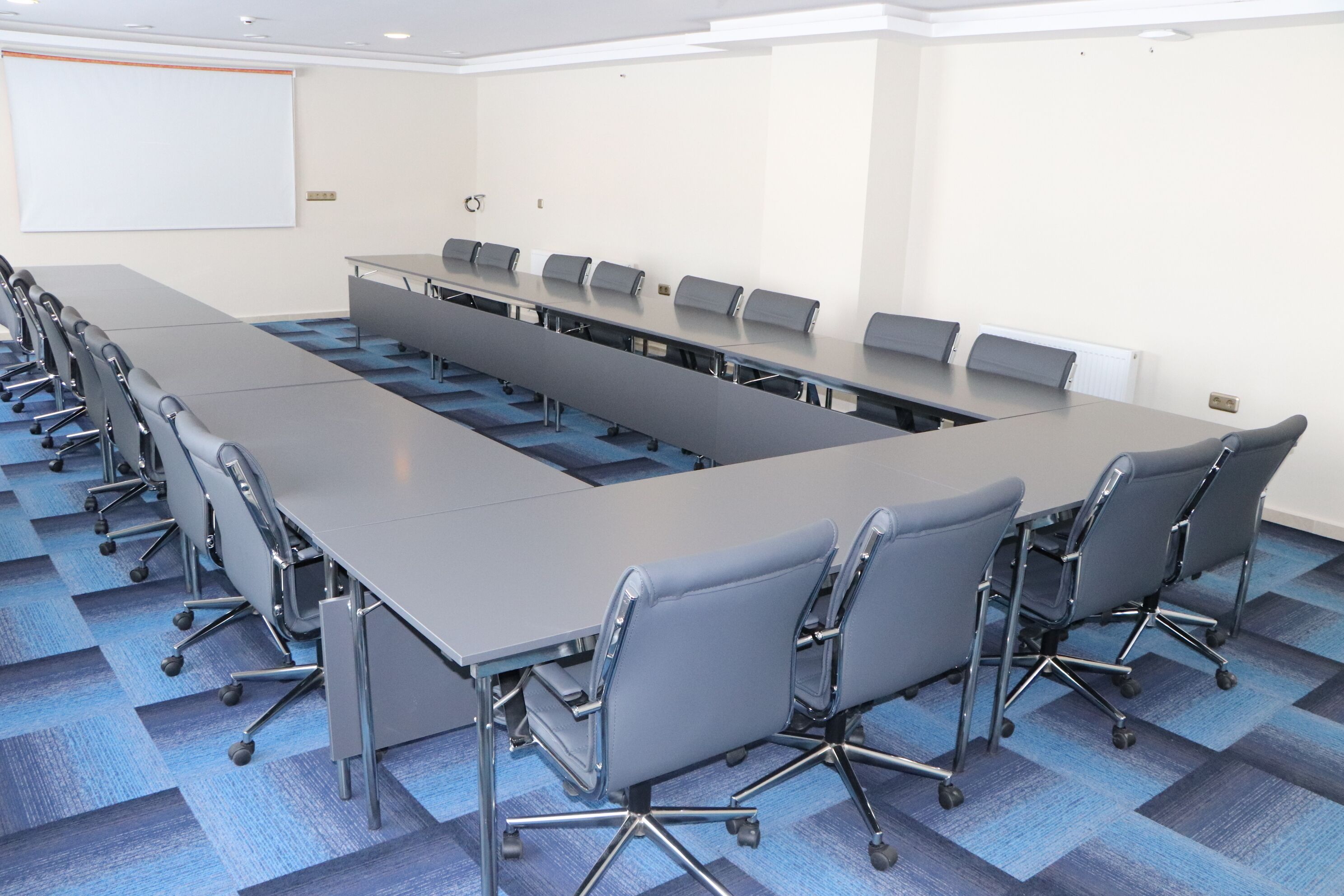 Un salón de conferencias con una larga mesa, sillas y una pantalla para proyector.