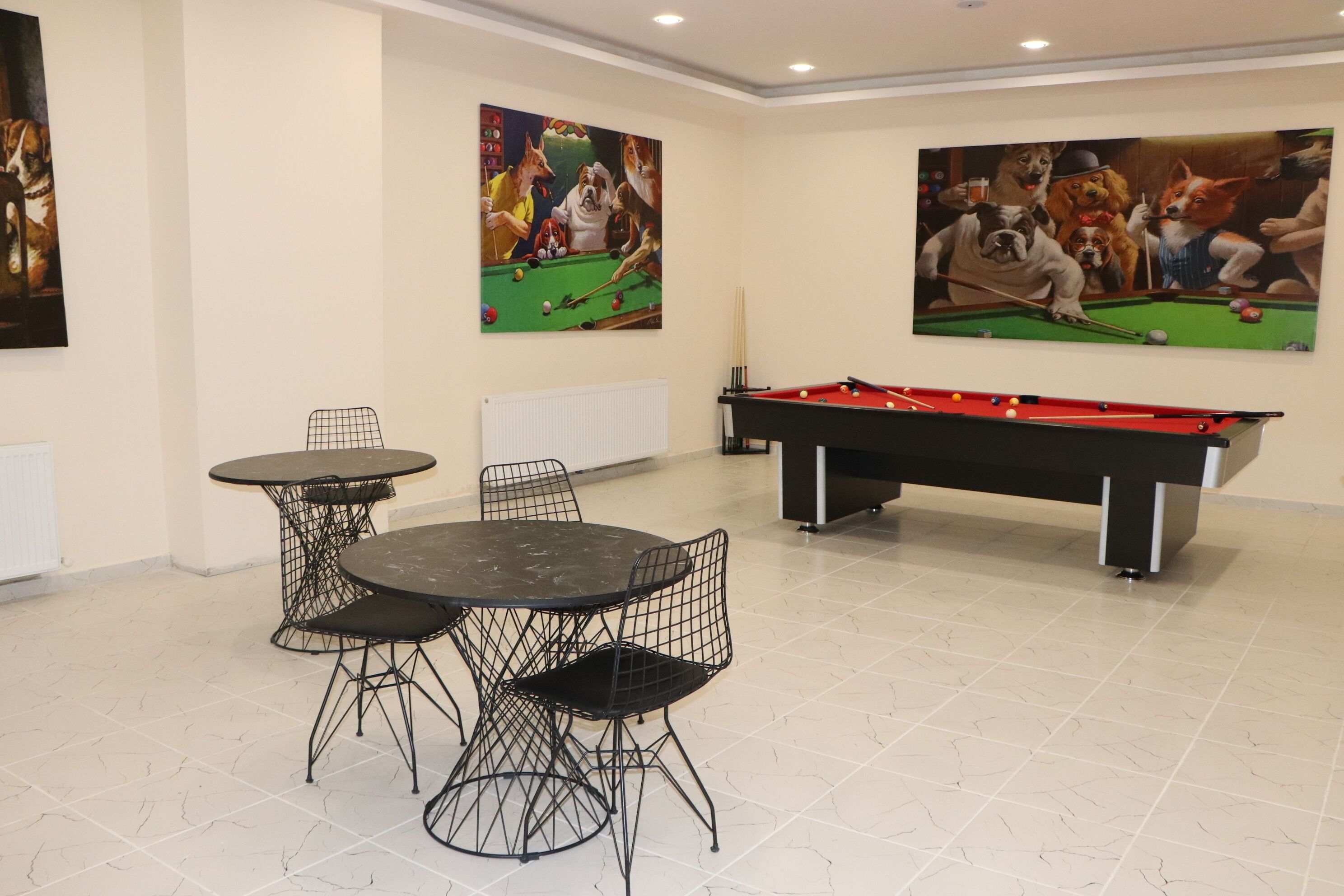 A pool table with a red cloth, two black wire chairs, and two round tables with black wire frames.