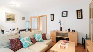 En stue med sofa, sofabord, TV-møbel og spiseområde med et bord dækket til to.