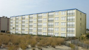 Et hotel med flere etager, fladt tag og altaner, beliggende på et sandet område med begrønning.