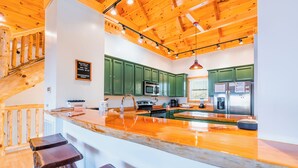 A modern kitchen with green cabinets, a wooden island with stools, and a stainless steel refrigerator.