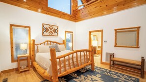 A bedroom with a wooden bed, a blue patterned rug, wooden walls, and a skylight.