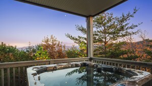 A hot tub on a wooden deck with a view of trees and mountains.