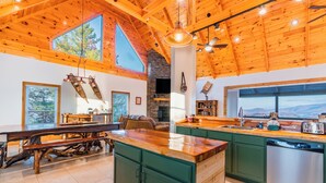 A spacious kitchen with a large island, green cabinets, and a stone fireplace.