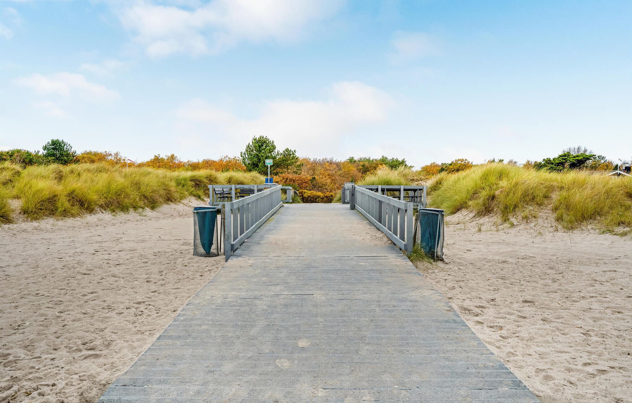 Een betonnen looppad dat naar een strand leidt, met zand en grasduinen aan beide zijden.
