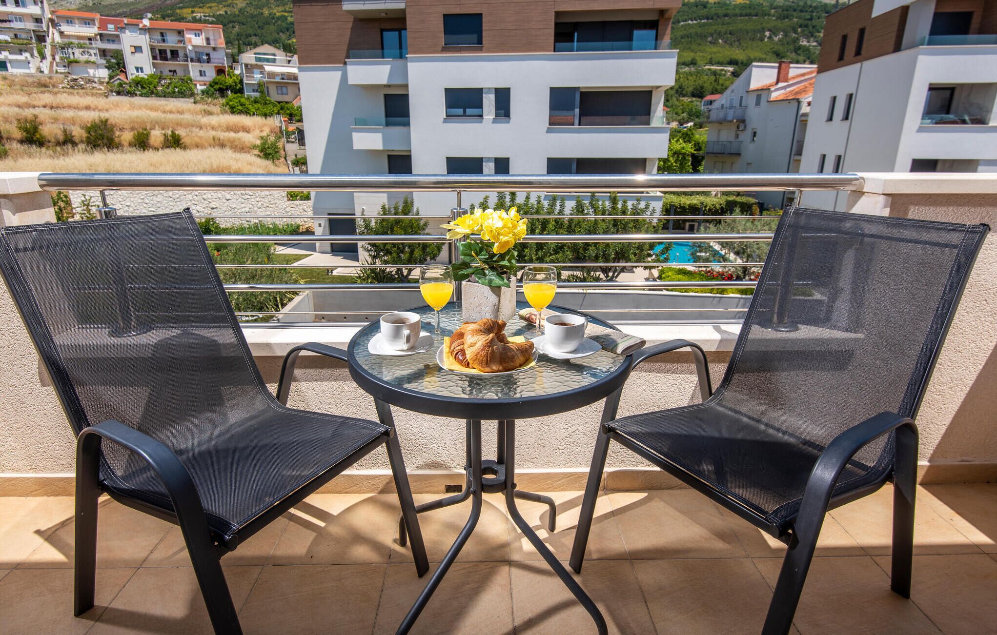 Een balkon met twee stoelen, een klein tafeltje en een vaas met gele bloemen.