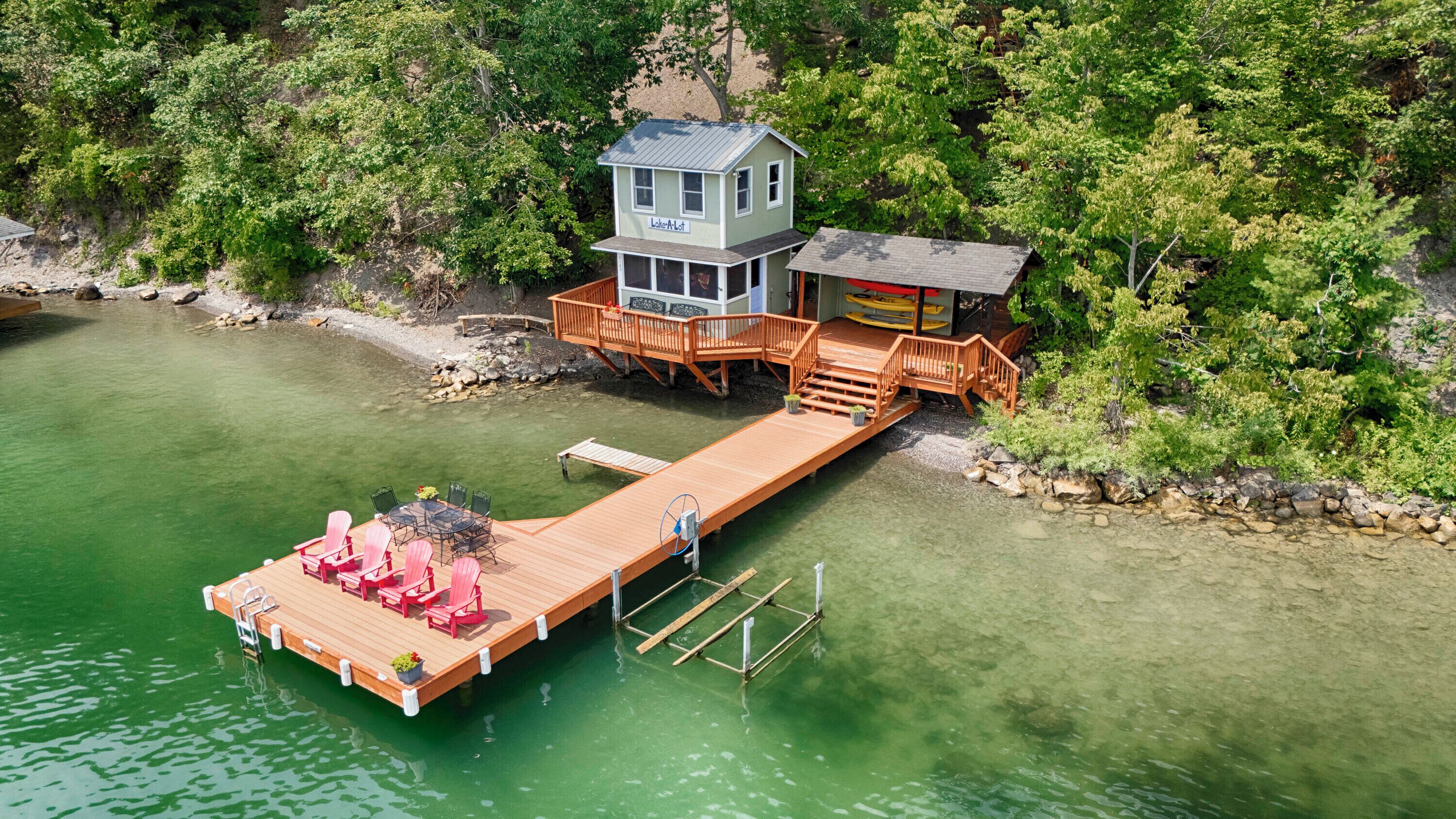 A lakeside cabin with a dock extending into the water, a deck with chairs, and a small shed.