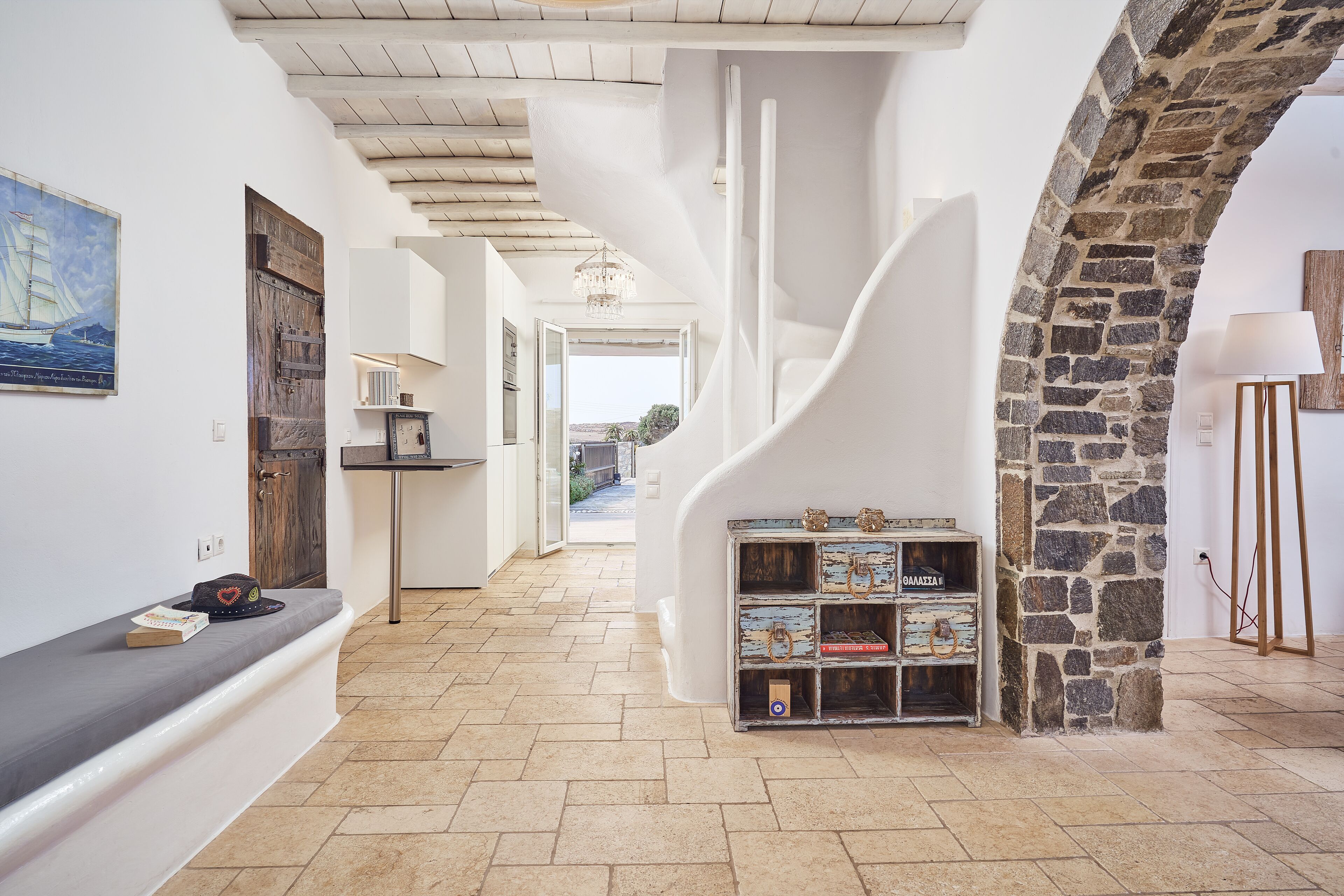 A hallway with a stone wall, a wooden door, and a view to the outside.