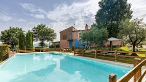 Una piscina con cerramiento de madera, un edificio con puertas azules y árboles al fondo.