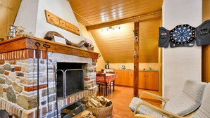 Ein gemütliches Zimmer mit Kamin aus Stein, einer Dartscheibe und einer Essecke mit Holzmöbeln.