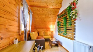 Ein gemütliches Blockhaushaus-Interieur mit Holzwänden und -decken, einer Couch, einem kleinen Tisch und einer Wand mit Grünpflanzen und Blumen.