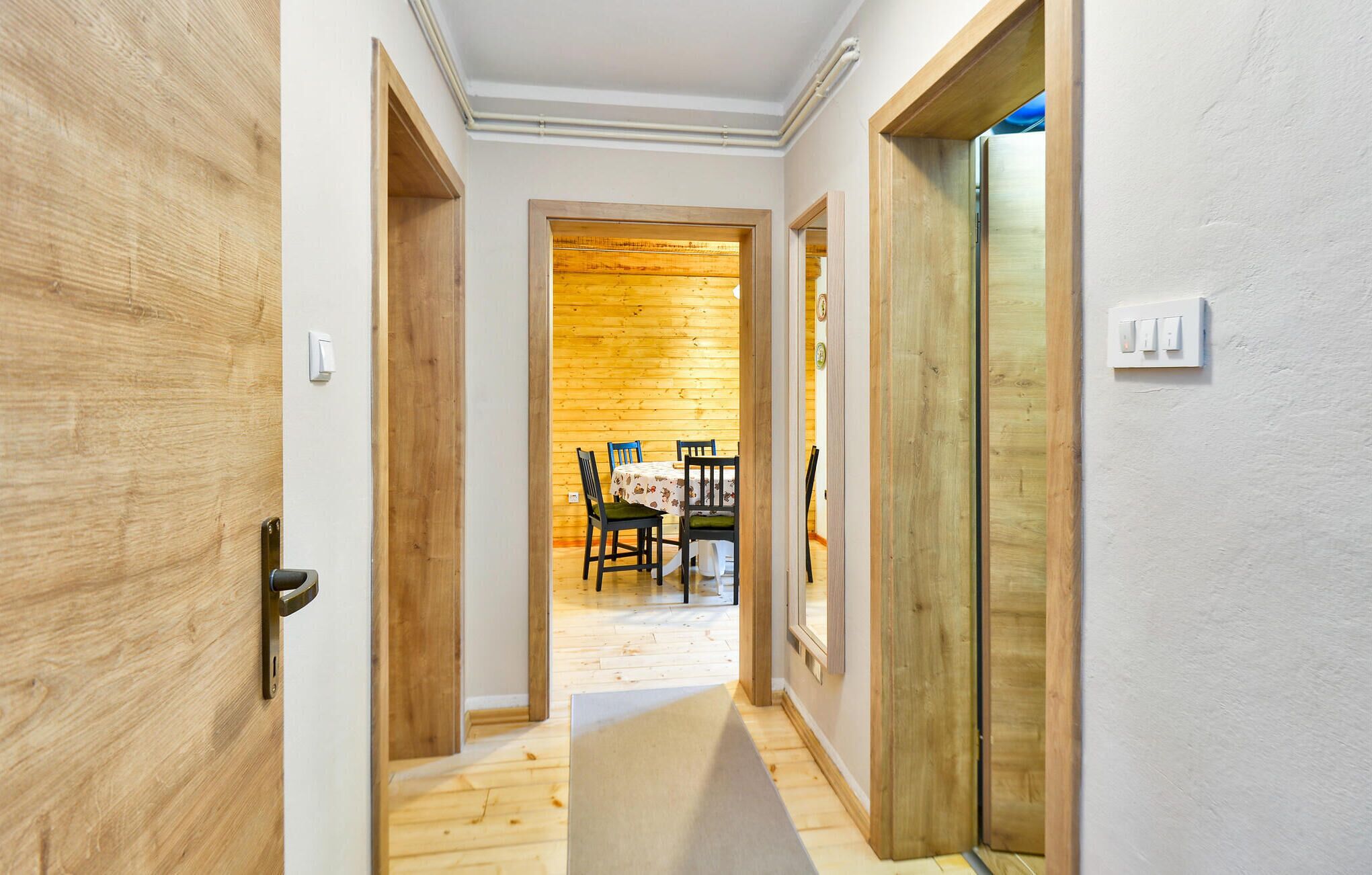 A hallway with wooden doors and walls, leading to a dining area with a table and chairs.