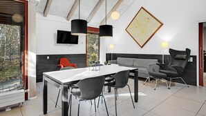 Un salon moderne avec une table blanche, un canapé gris et des chaises noires. Un téléviseur est fixé au mur et une grande peinture abstraite est accrochée au-dessus du canapé.