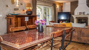 A dining area with a mosaic table, wooden chairs, a vase with flowers, a television, and a fireplace with the word "LOVE" on it. - Stunning home in ROUJAN (ROUJAN)