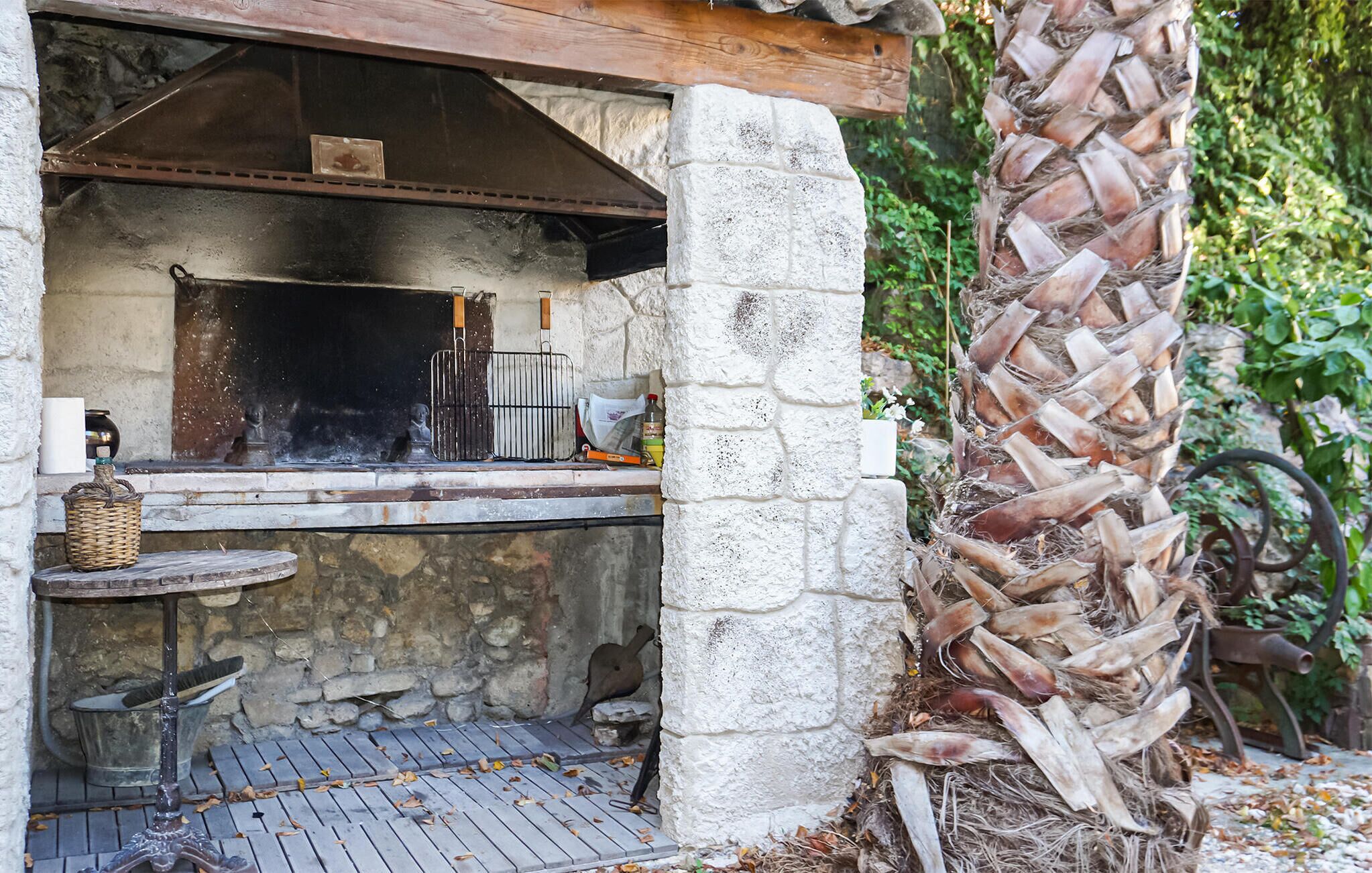 Una cucina esterna con parete in pietra, griglia in metallo e tavolo rustico in legno.