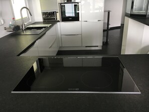 A modern kitchen with a black induction cooktop, a built-in oven, and a toaster.