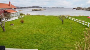 A grassy yard with a white fence, a small tree, and a house with a red roof. - 3 bedroom cozy home in Lindesnes (Lindesnes)