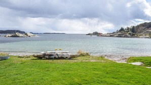 A lakeside view with a grassy foreground, a wooden log, and a small table with flowers. - 3 bedroom cozy home in Lindesnes (Lindesnes)