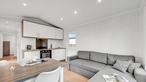 Una cocina moderna con armarios blancos, una mesa de comedor con sillas y un sofá gris con una revista.