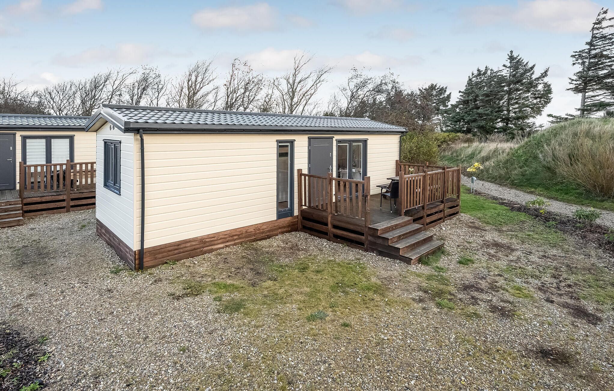 A small, single-story mobile home with a wooden deck and a door leading to a covered porch.