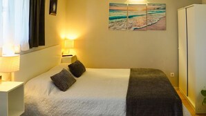 Ein Schlafzimmer mit einem Bett, zwei Kissen, einem Nachttisch mit Lampe, einem Wandbild und einem Kleiderschrank.