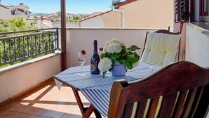 Ein Balkon mit Tisch für zwei Personen, einem Blumentopf und einer Weinflasche.