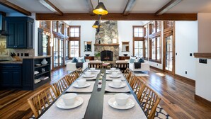 Uma sala de jantar espaçosa com uma mesa comprida posta para uma refeição, ladeada por cadeiras de madeira e uma lareira de pedra.