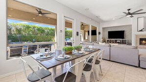 Una cocina moderna con zona de comedor, ventanas amplias, ventiladores de techo y televisor.