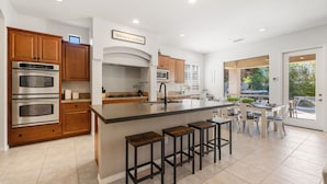 Una cocina moderna con una isla central, hornos empotrados, armarios de madera y una zona de asientos con taburetes de bar.