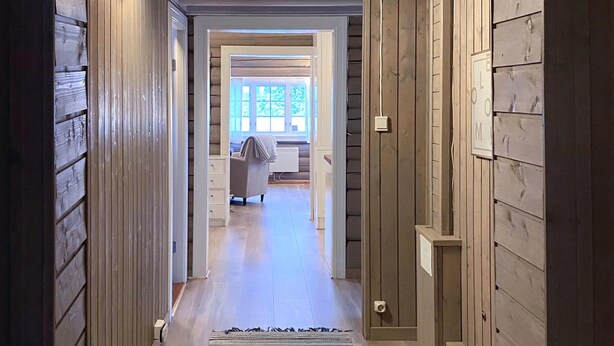 Ein Flur mit Holzwänden und einem Teppich, der zu einem Zimmer mit einem Bett und einem Fenster führt.
