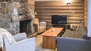 Ein gemütliches Blockhaus-Interieur mit Kamin aus Stein, einem Fernseher und bequemen Sitzgelegenheiten.