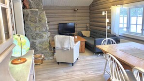 Ein gemütliches Blockhaus-Interieur mit einer Steinwand, einem Fernseher, einer Couch und einem Essbereich.